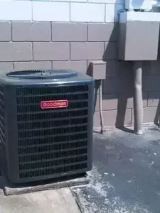 Goodman air conditioning unit installed outside a commercial building with a concrete block wall and electrical service panel nearby.