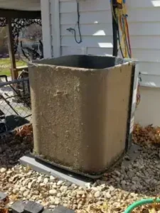 Dirty outdoor AC unit coil needing maintenance next to house, exposed wiring and debris visible.