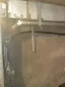 Double-wall insulated HVAC ductwork installation in unconditioned basement space with metal brackets and exposed concrete walls.